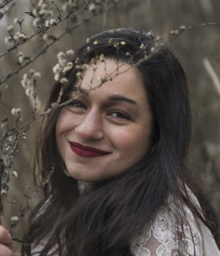 Women with long brown hair smiling in woods.