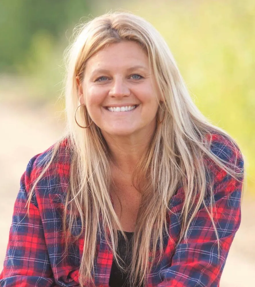 Women with long blonde hair wearing flannel shirt smiling with nature background.