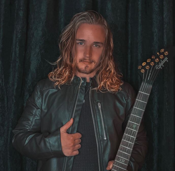 Man on dark background holding guitar with leather jacket.